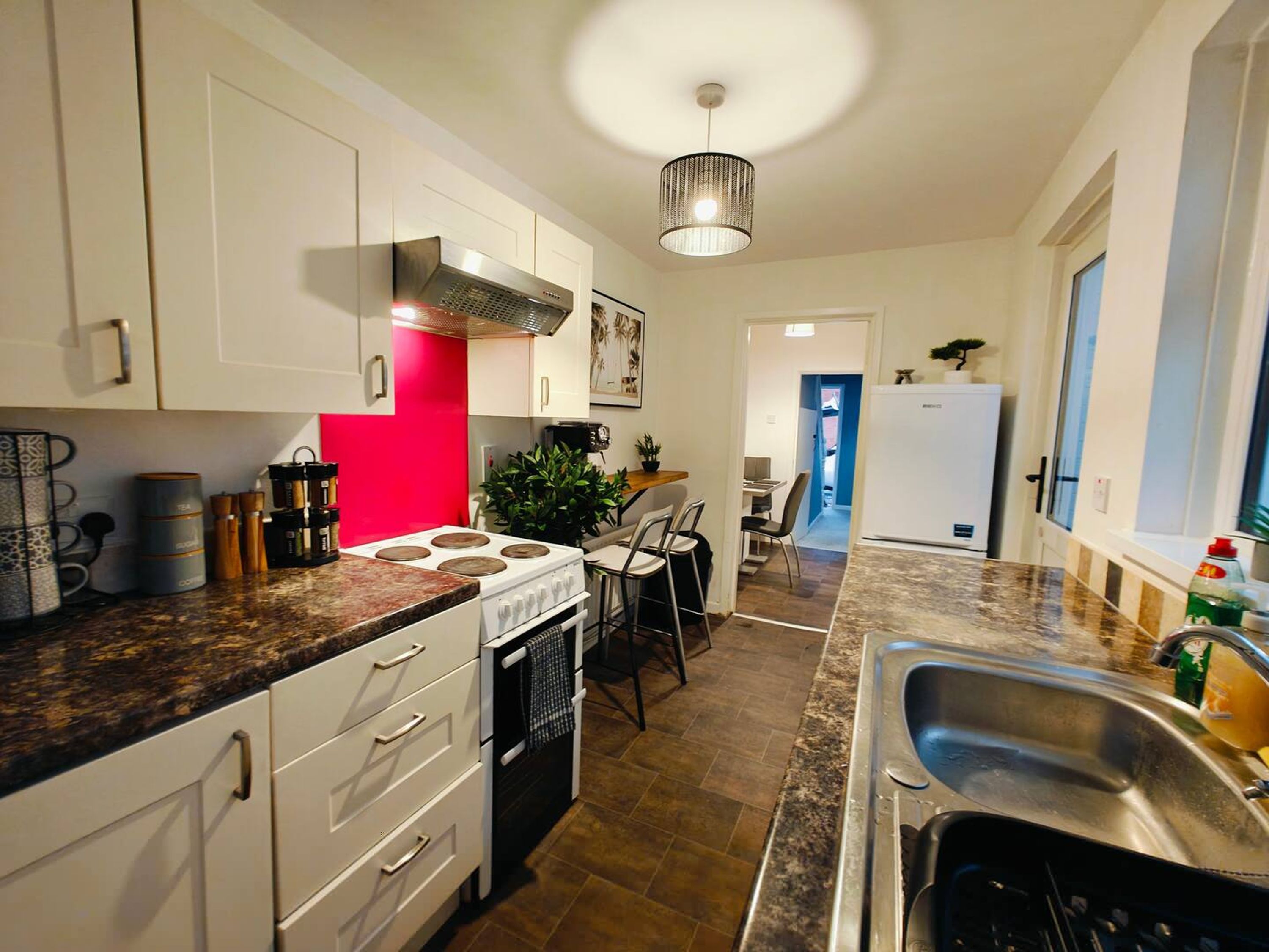 Una cocina moderna con armarios blancos, una pared de acento roja, una estufa a gas, un fregadero y un comedor con sillas.