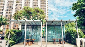 A covered outdoor seating area with tables and benches, surrounded by greenery and a tall residential building in the background. - Studio Unit W/ Balcony•Sea & City View (Lapu-Lapu)
