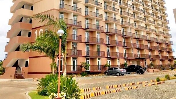 A high-rise residential building with multiple balconies, a staircase on the left, and a parking area in front. - Studio Unit W/ Balcony•Sea & City View (Lapu-Lapu)