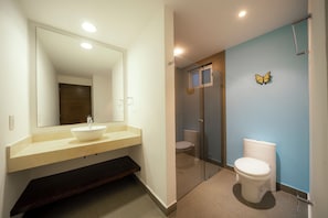 Un baño moderno con un espejo grande, un lavamanos, un inodoro y una zona de ducha.
