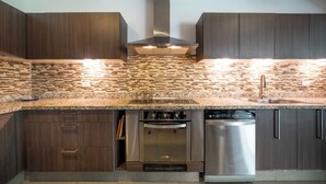 A modern kitchen with dark wood cabinets, a stainless steel range hood, a built-in oven, and a dishwasher. - Vaiven 124 - 2 Recamaras 4 Piscinas (Playa del Carmen)