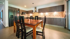A modern kitchen with a wooden dining table and chairs, a built-in microwave, and a stainless steel refrigerator. - Vaiven 124 - 2 Recamaras 4 Piscinas (Playa del Carmen)