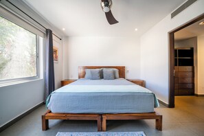 Un dormitorio moderno con una cama de madera, un ventilador de techo, un ventanal con cortinas y vistas al exterior.