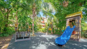 A playground with a blue slide, a climbing structure, and a wooden playhouse. - Vaiven 124 - 2 Recamaras 4 Piscinas (Playa del Carmen)