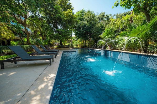 Una piscina con sillas de descanso y una cascada, rodeada de exuberante vegetación.