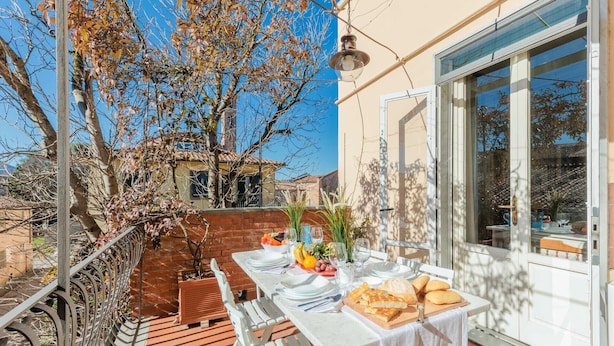 Una terraza con mesa lista para comer, una planta en maceta y vistas del entorno.
