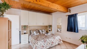 Una camera da letto con soffitto in legno, un letto con biancheria da letto floreale, un armadio e una finestra con tende.