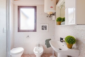 Un bany amb vàter, bidet i rentapel, una finestra i un mirall amb una planta.