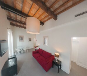 Un grand salon comprenant un canapé rouge, une table à manger avec des chaises, une lampe et un ventilateur de plafond.