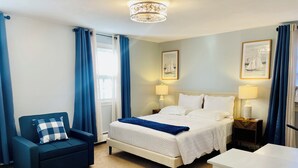 Habitación de hotel con cama, una silla, dos mesitas de noche con lámparas y dos cuadros en la pared.