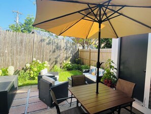 Un patio al aire libre con mesa y sillas, un gran paraguas y una valla de madera al fondo.