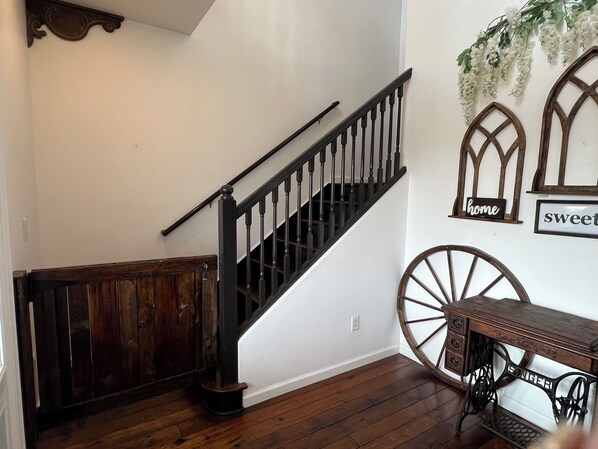 A wooden staircase with a black handrail, a vintage sewing machine, and decorative wall art.