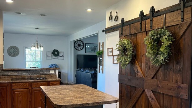 A kitchen with a large island, wooden cabinets, and a barn-style door with wreaths.
