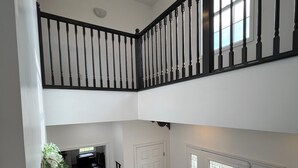A multi-level interior with a staircase, a chandelier, and a door with stained glass.