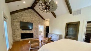 Un dormitorio con una cama grande, una pared de piedra, una chimenea, un televisor y un ventilador de techo.