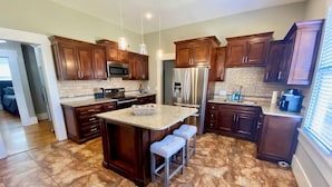 Una cocina moderna con armarios de madera oscura, electrodomésticos de acero inoxidable y una isla con encimera de granito y taburetes de bar.