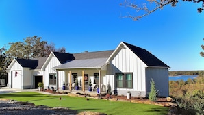 A modern house with a covered porch, a lawn, and a view of a lake.