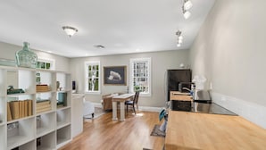 Una cocina moderna con encimera de madera, un comedor con mesa y sillas, y un estante blanco con diversos objetos.
