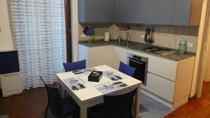 A compact kitchen with grey cabinets, a white countertop, and a dining area with a table and chairs. - The Dream Fisherman: a cozy nest in the center of town  (Pescara)