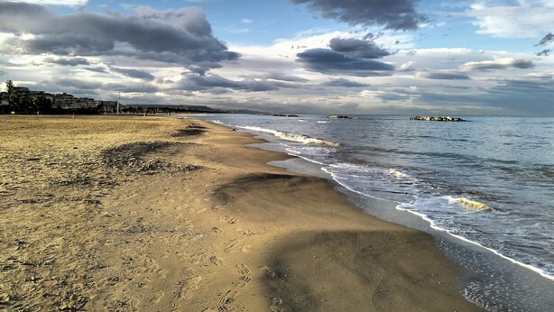 A beach with footprints leading to the water, a rocky breakwater, and buildings in the background. - The Dream Fisherman: a cozy nest in the center of town  (Pescara)