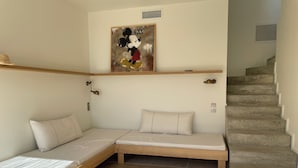 Une pièce avec un lit en bois, un petit canapé, un tableau représentant Mickey Mouse et un escalier.