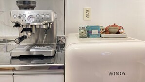Une cuisine équipée d’une machine à café et d’un appareil électroménager blanc, peut-être un réfrigérateur ou un four, avec un bocal et une boîte posés sur le plan de travail.