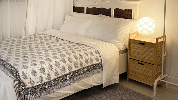 Un lit bien fait, recouvert d’une couverture à motifs, avec une lampe de chevet et une table de nuit en bois.
