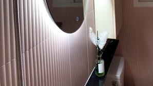 Une salle de bain avec un grand miroir, une douche, des toilettes et un lavabo.