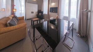 Un salon moderne avec un plafond en bois, une table à manger en verre, un canapé et un téléviseur fixé au mur.