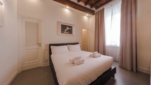 Une chambre à coucher avec un lit, une porte, un tableau encadré au mur et une fenêtre avec des rideaux.