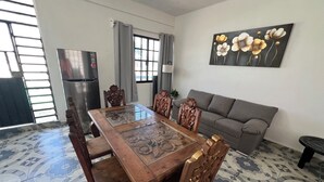 Un comedor con una mesa y sillas de madera, un sofá gris y un cuadro de flores en la pared.