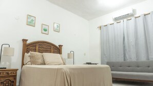 Un dormitorio con cama, mesitas de noche, un sofá gris y una ventana con cortinas.
