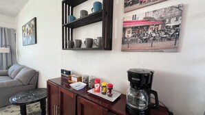 Un espacio de estar con un sofá, una mesa de centro y un mueble de madera con una cafetera y condimentos.