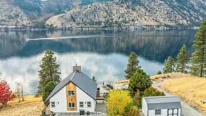 A house with a wooden front door, a garage, and a view of a lake with mountains in the background. - NEW! Gorgeous lake home w/ private pool, hot tub, lake access with dock & views! (Manson)