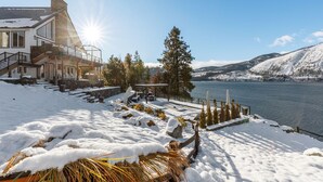 A snow-covered landscape with a house overlooking a lake, featuring a balcony and outdoor seating area. - NEW! Gorgeous lake home w/ private pool, hot tub, lake access with dock & views! (Manson)