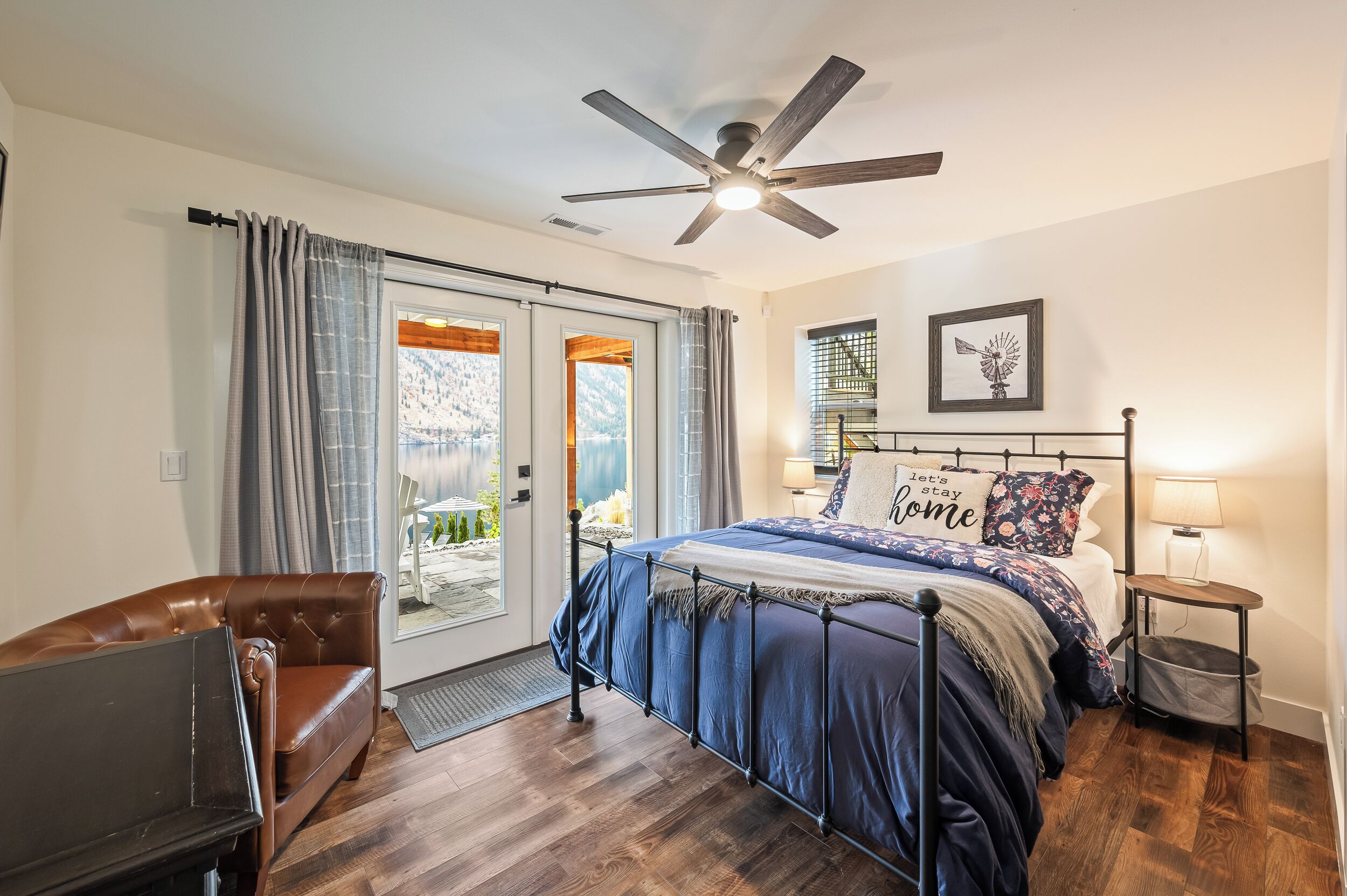 A bedroom with a bed, a ceiling fan, a nightstand, a lamp, and a view through the door.