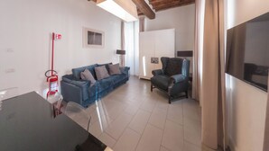 A living room with a blue sofa, a black armchair, a flat-screen TV, and a wooden ceiling. - Vatican Mascherino suite (MAS-2) (Roma)