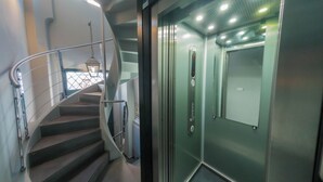 A modern elevator with a metallic finish, a glass door, and a control panel with a red button. - Vatican Mascherino suite (MAS-2) (Roma)
