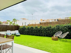 An outdoor patio with a table and chairs, a well-maintained lawn, and a bamboo fence. - Apartment with large terrace in Punta Prima, (VC)