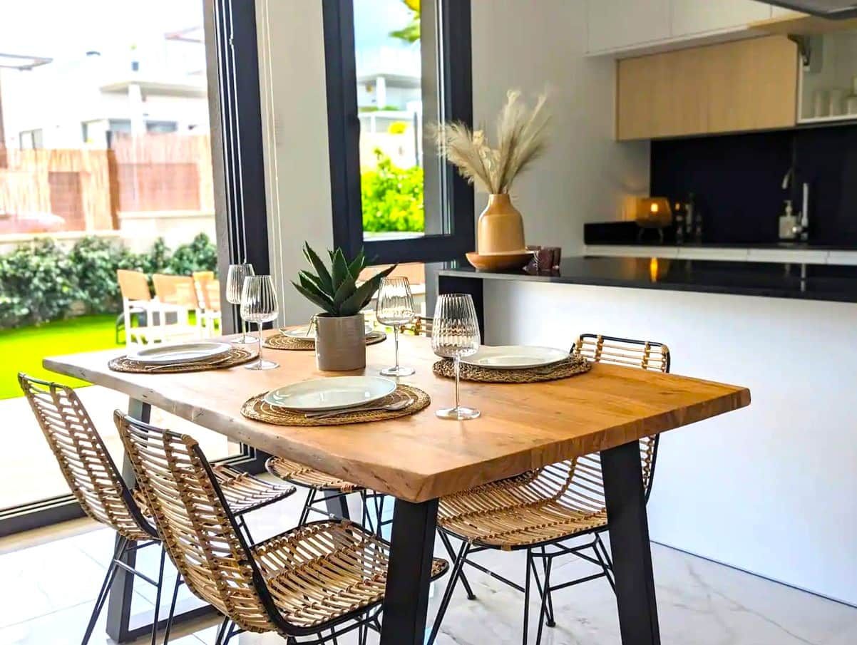 A dining area with a wooden table set for four, surrounded by wicker chairs.