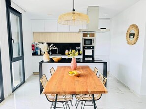 A modern kitchen with white cabinetry, a wooden dining table, and a central island with a vase and flowers. - Apartment with large terrace in Punta Prima, (VC)