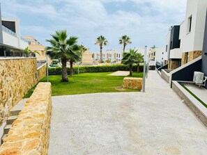 A modern residential area with a paved walkway, stone walls, and palm trees. - Apartment with large terrace in Punta Prima, (VC)