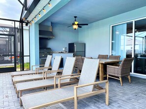 An outdoor patio with a dining table and chairs, a grill, and a ceiling fan. - Toy Story Slide • Guardians Theater • Themed Rooms • Pool & Spa • Grill • Arcade (Davenport)