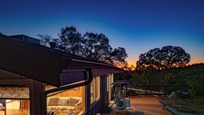 Een gezellig terras buiten met een bank en stoelen, een eettafel en uitzicht op de zonsondergang.