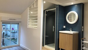 A modern bathroom with a glass shower, a wooden vanity, and a large window with a view of a street.