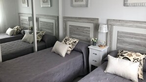 Une chambre à coucher avec deux lits, chacun recouvert d’une couverture grise et agrémenté d’oreillers à motifs. On y trouve des tables de chevet avec des lampes et des œuvres d’art décoratives accrochées au mur.