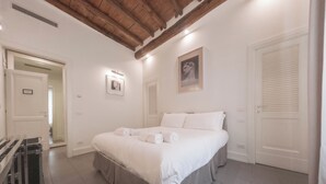 Un dormitorio con una cama grande, techo de madera, paredes blancas y una puerta con ventanal.