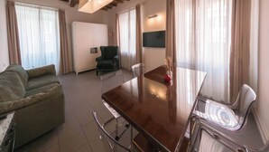 Un amplio salón con techo de madera, un sofá, una mesa de comedor con sillas y un televisor montado en la pared.
