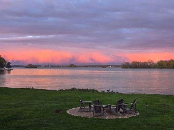 A lakeside view with chairs and tables on a grassy area.