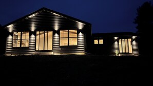 A two-story wooden cabin with large windows, a sloped roof, and exterior lighting. - Modern Lake Home: Family Fun & Memorable Getaway! (Beaver Dam)